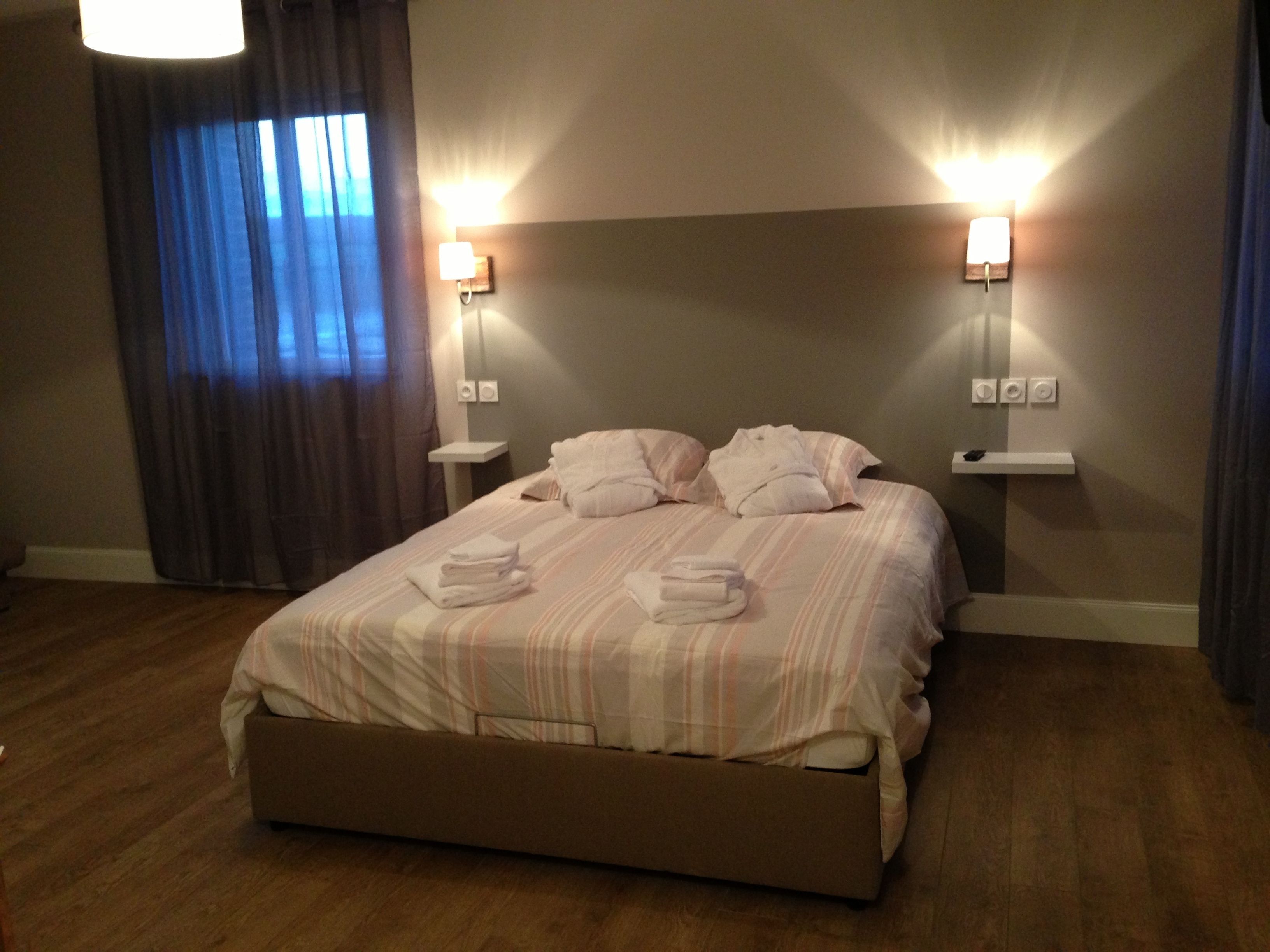 A hotel room with a large bed, two bedside tables, a nightstand, a lamp, and a window with curtains.