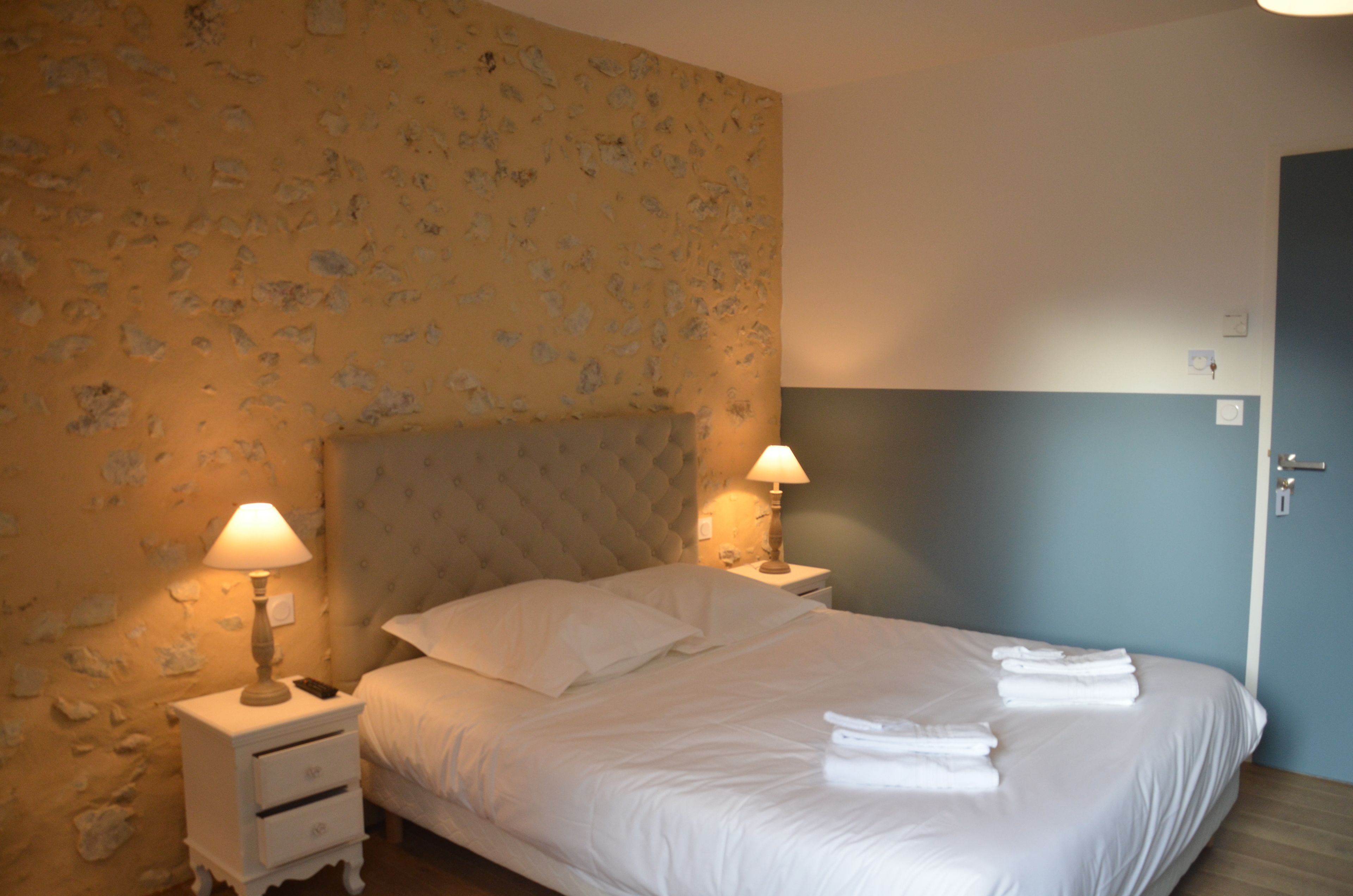 A hotel room with a bed, two bedside lamps, a nightstand, and a wall with a floral pattern.