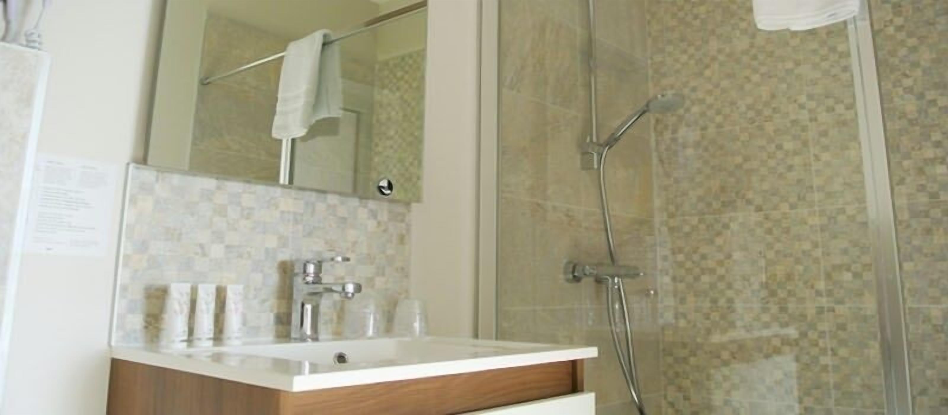 A bathroom with a glass shower enclosure, a white sink with a wooden vanity, and a mirror above the sink.