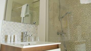 A bathroom with a glass shower enclosure, a white sink with a wooden vanity, and a mirror above the sink.