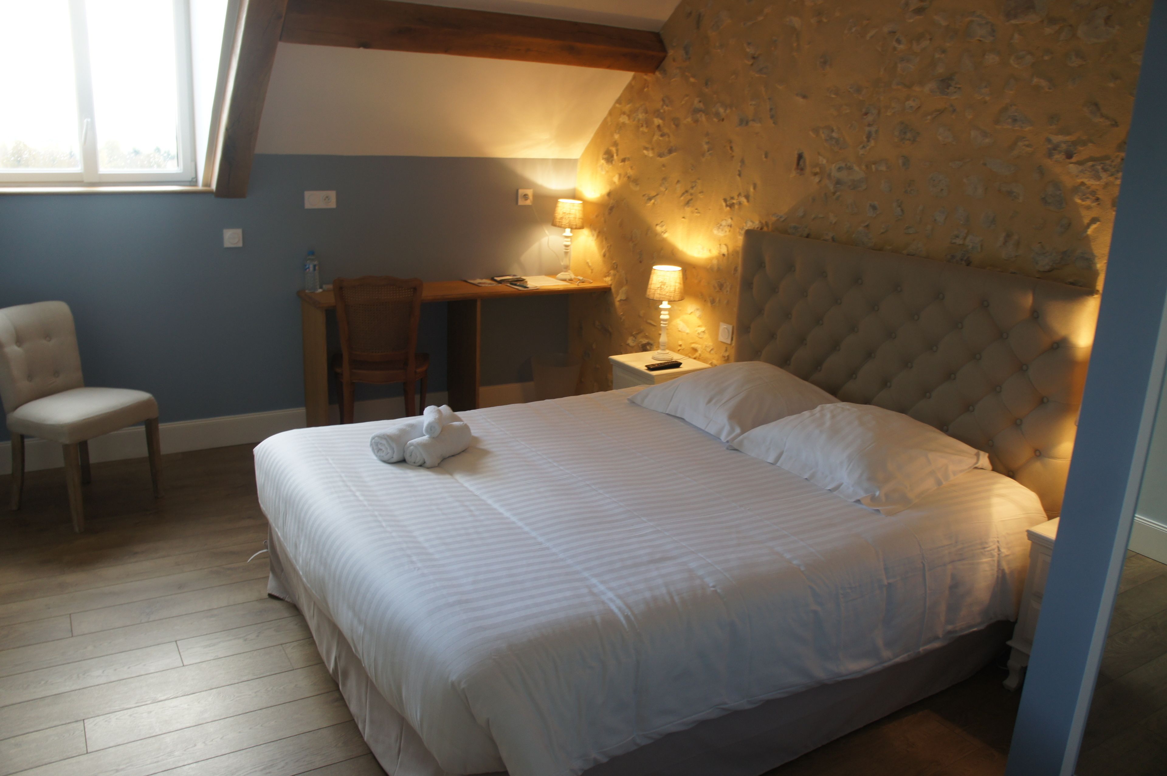 A bedroom with a large bed, a desk, a chair, and two bedside lamps.