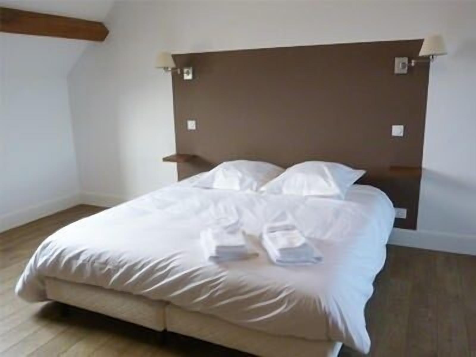 Una cama bien tendida con sábanas y almohadas blancas, un cabecero de madera y dos lámparas de noche.