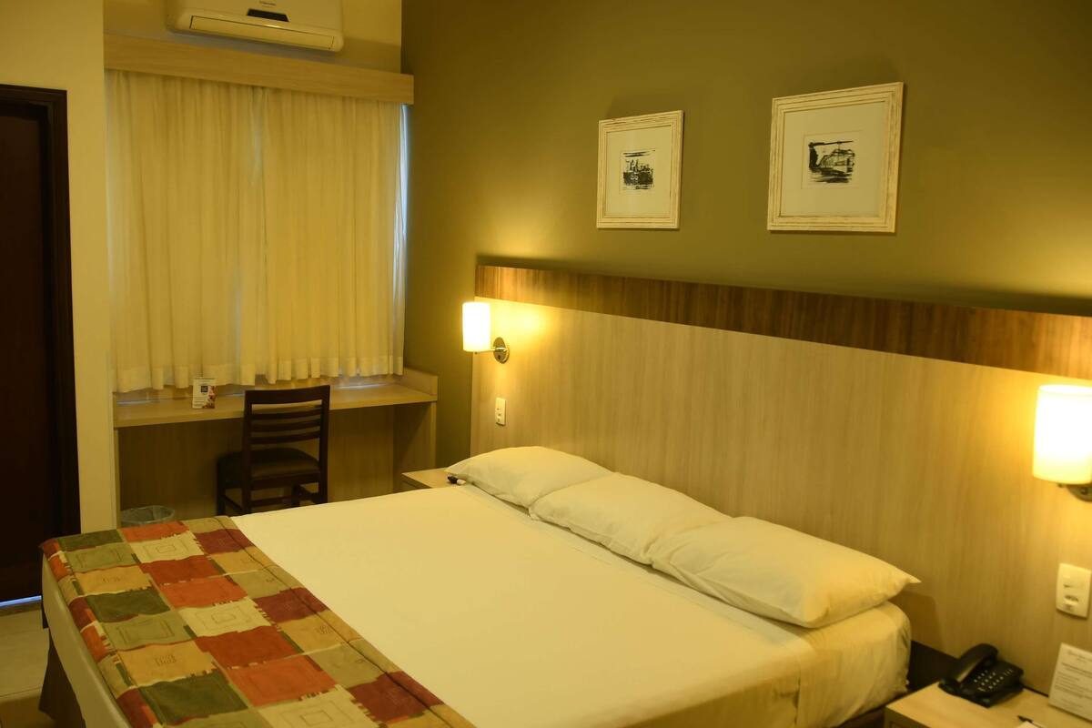 Habitación de hotel con cama, escritorio, silla, mesita de noche y dos lámparas de pared.