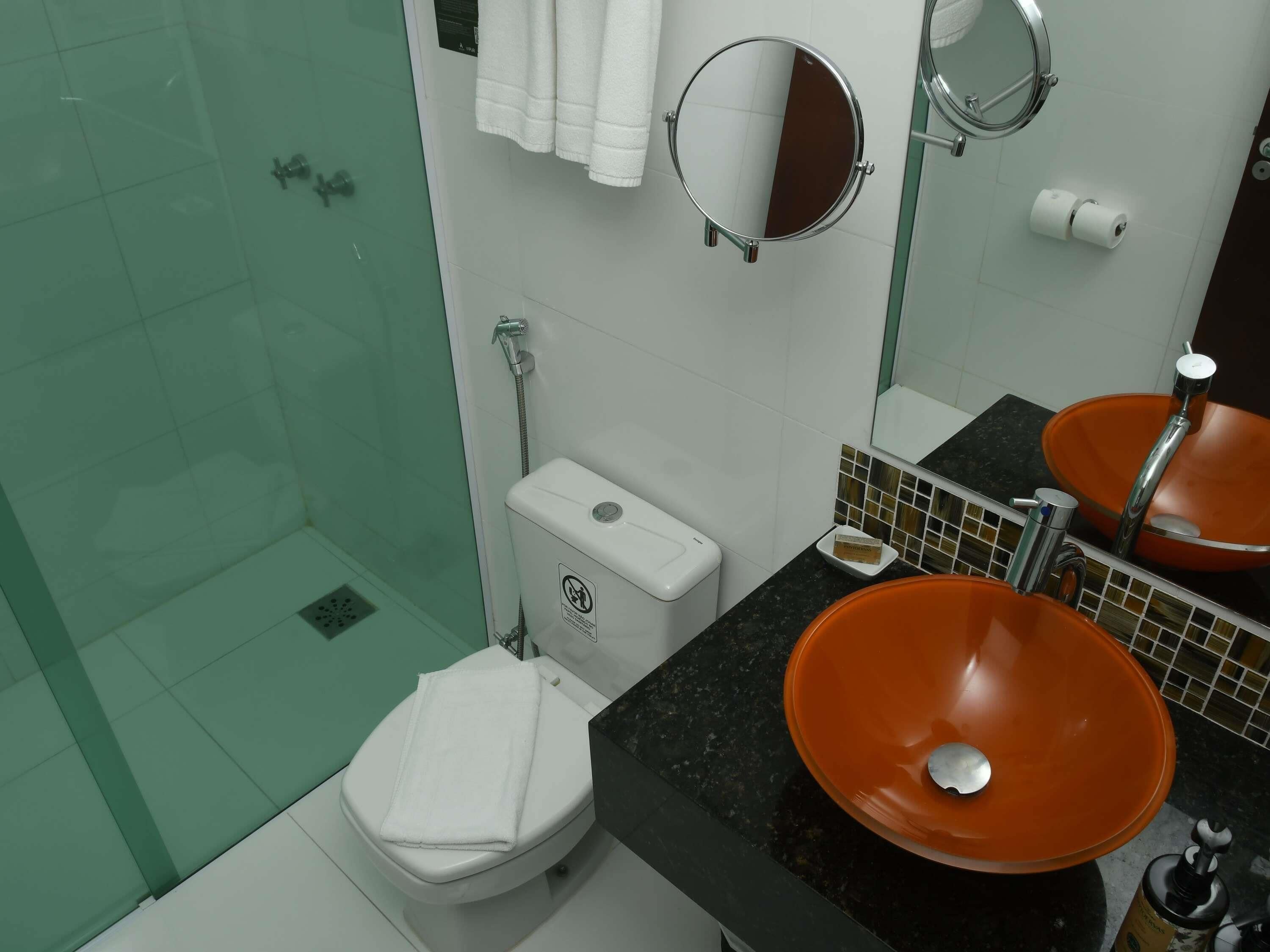 A bathroom with a toilet, a sink with an orange basin, a shower area, and a mirror.