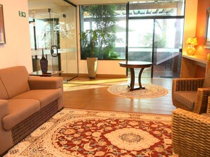 A modern hotel lobby with a sofa, a small table, a large potted plant, and a view of the outdoors. - Hotel Araraquara by Mercure (Araraquara)