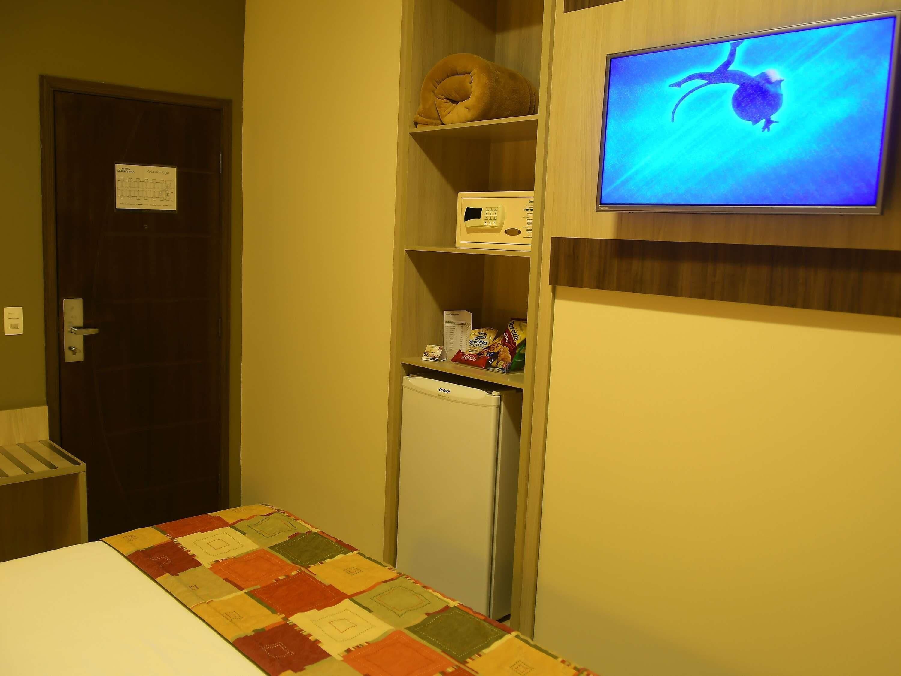 Una habitación pequeña con una cama, refrigerador, microondas y televisión en la pared.