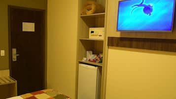 Una habitación pequeña con una cama, refrigerador, microondas y televisión en la pared.