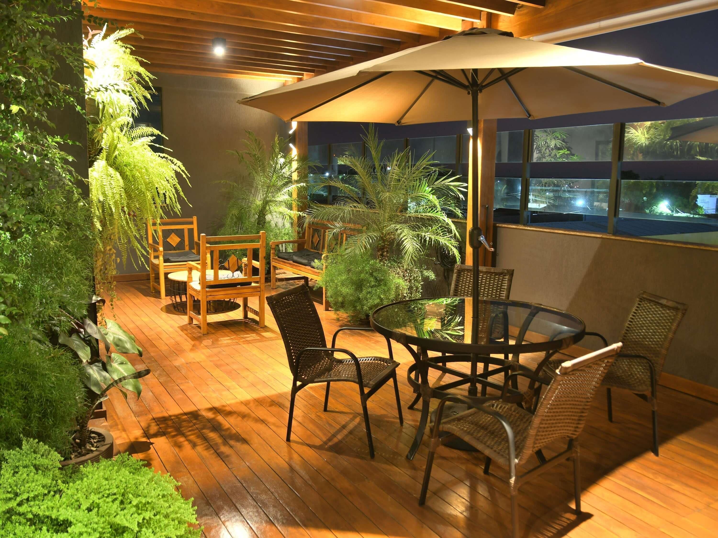An outdoor patio with wooden flooring, a round table, wicker chairs, and a large umbrella.