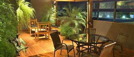 An outdoor patio with wooden flooring, a round table, wicker chairs, and a large umbrella.