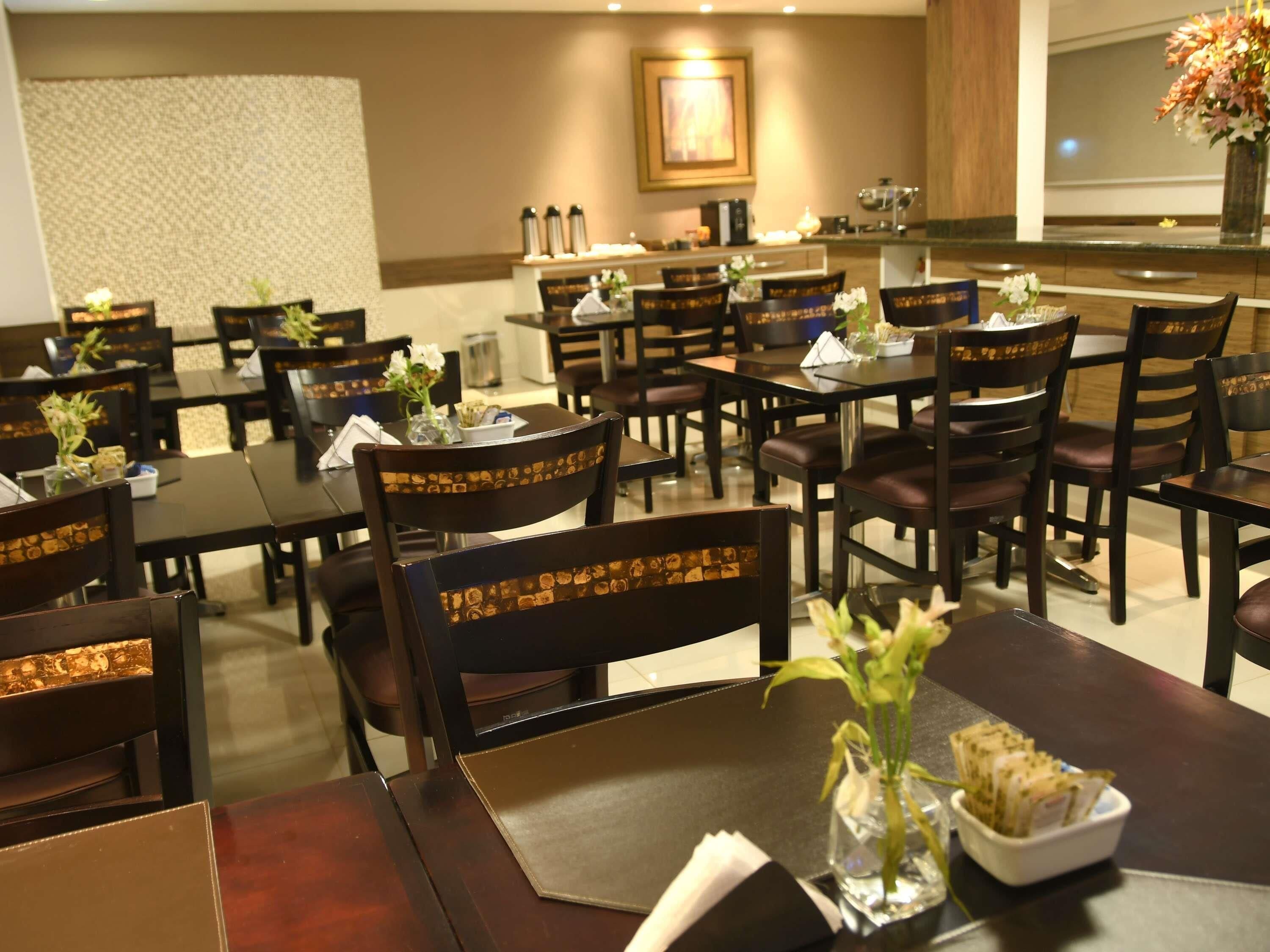 A hotel dining area with multiple tables and chairs, some with floral centerpieces.