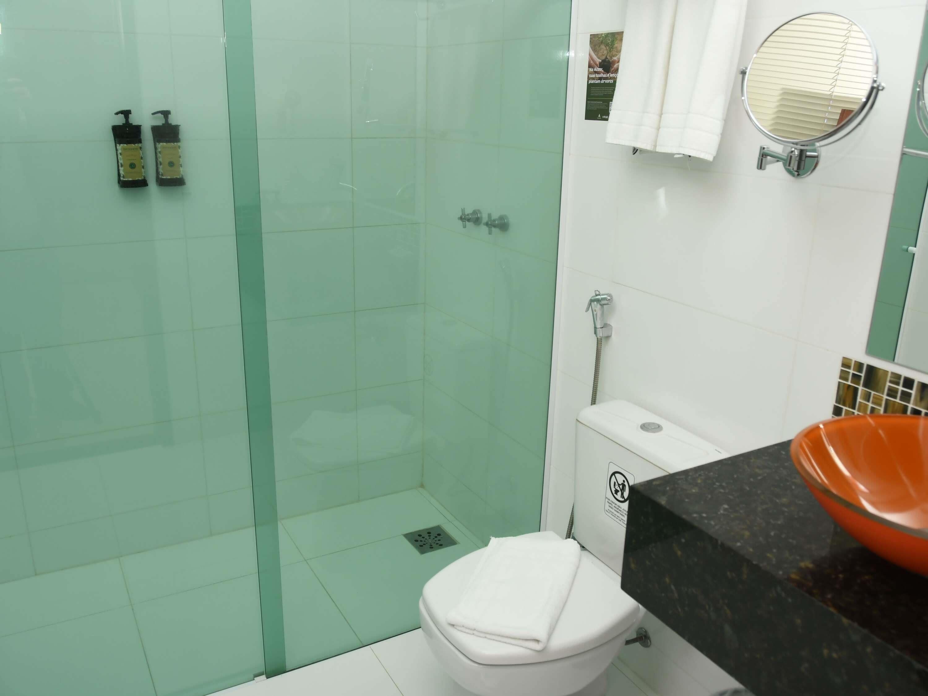 A bathroom with a glass-enclosed shower, a white toilet, and a black countertop with an orange sink.
