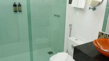 Une salle de bain avec une douche à parois de verre, des toilettes blanches et un plan de toilette noir avec un lavabo orange.