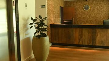 Un área de recepción con un mostrador de madera, una planta grande en maceta y un reloj en la pared.