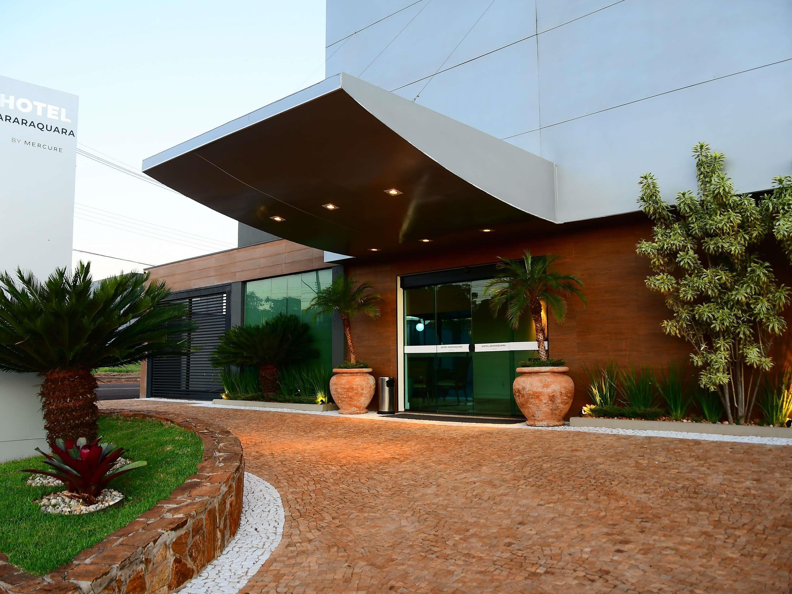 A modern hotel entrance with a covered walkway, large potted plants, and a well-maintained lawn.