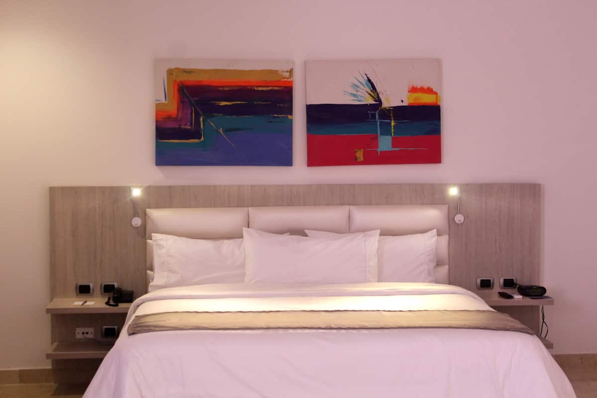 Ein modernes Hotelzimmer mit einem großen Bett, zwei Nachttischen und zwei abstrakten Bildern an der Wand.