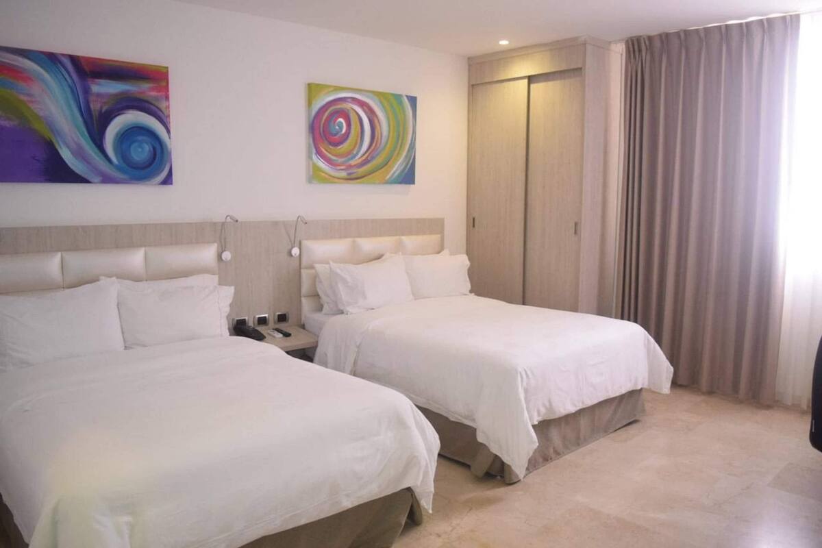 Ein Hotelzimmer mit zwei Betten, einem Kleiderschrank und zwei abstrakten Bildern an der Wand.