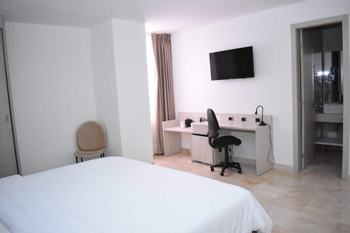 Ein Hotelzimmer mit Bett, Schreibtisch, Stuhl, Fernseher und einem durch eine offene Tür einsehbaren Badezimmer.