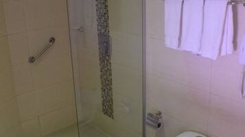 A bathroom with a glass-enclosed shower, a toilet, and a towel rack with folded towels.