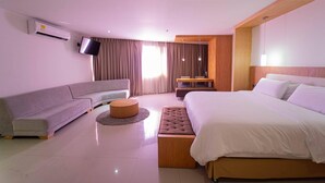 A modern hotel room with a large bed, a sofa, a TV, and an air conditioning unit. - Radisson Hotel Diamond Barranquilla (Barranquilla)
