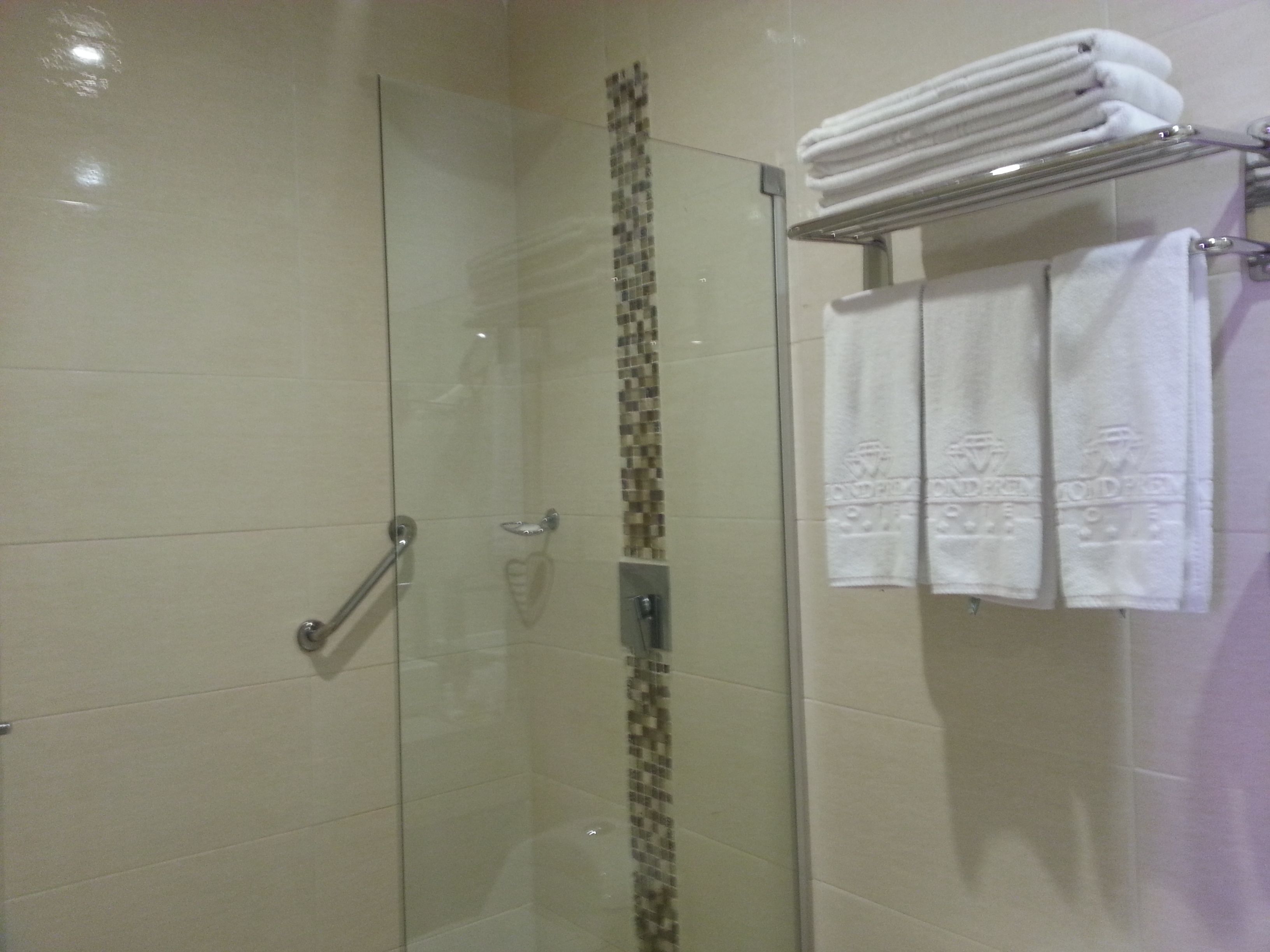A glass-enclosed shower with a tiled wall, a towel rack with folded towels, and a handrail.