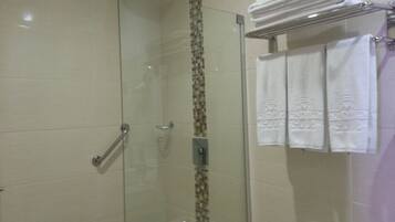 A glass-enclosed shower with a tiled wall, a towel rack with folded towels, and a handrail.