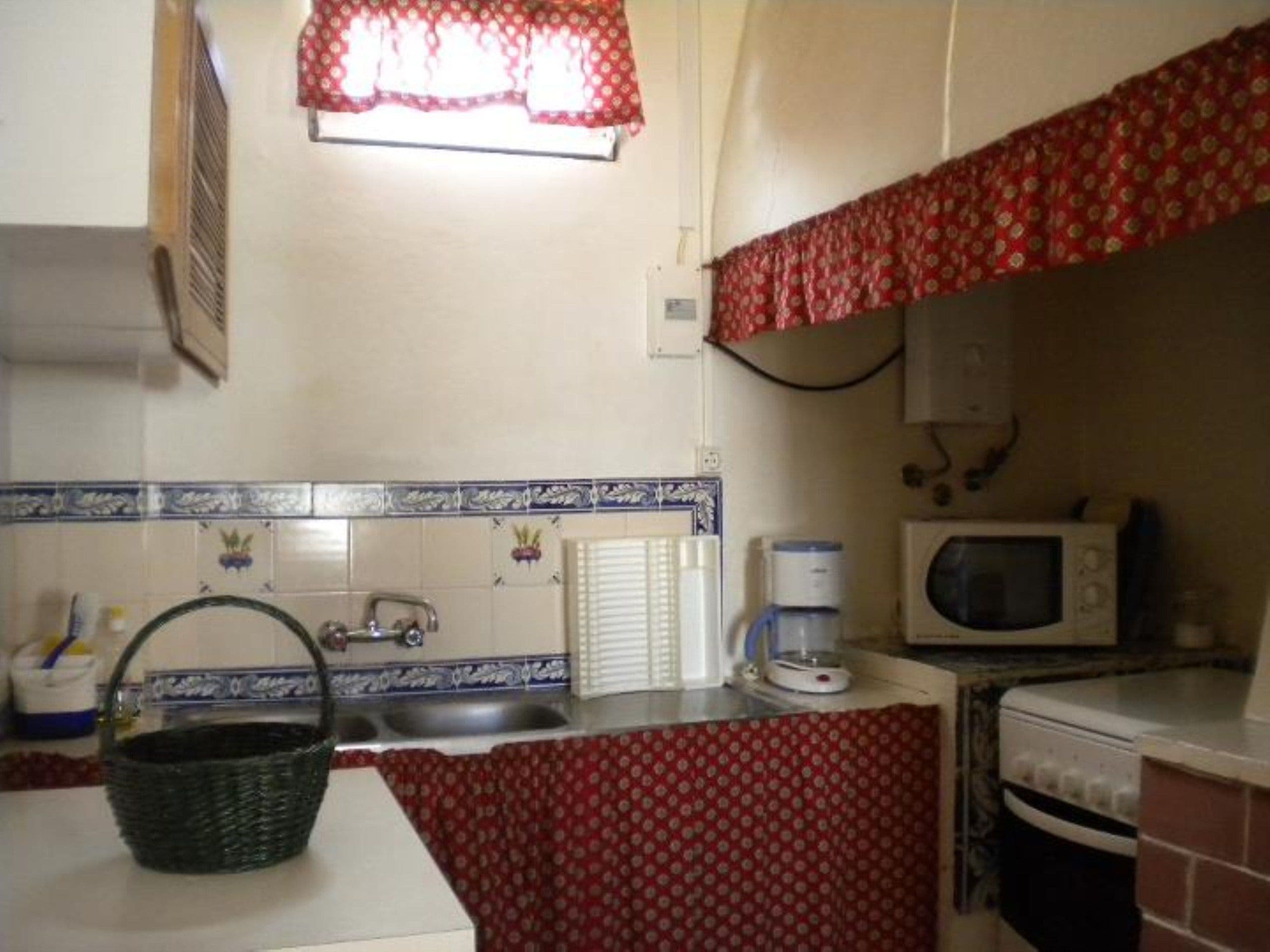 A compact kitchen with a sink, a microwave, a coffee maker, and a basket.