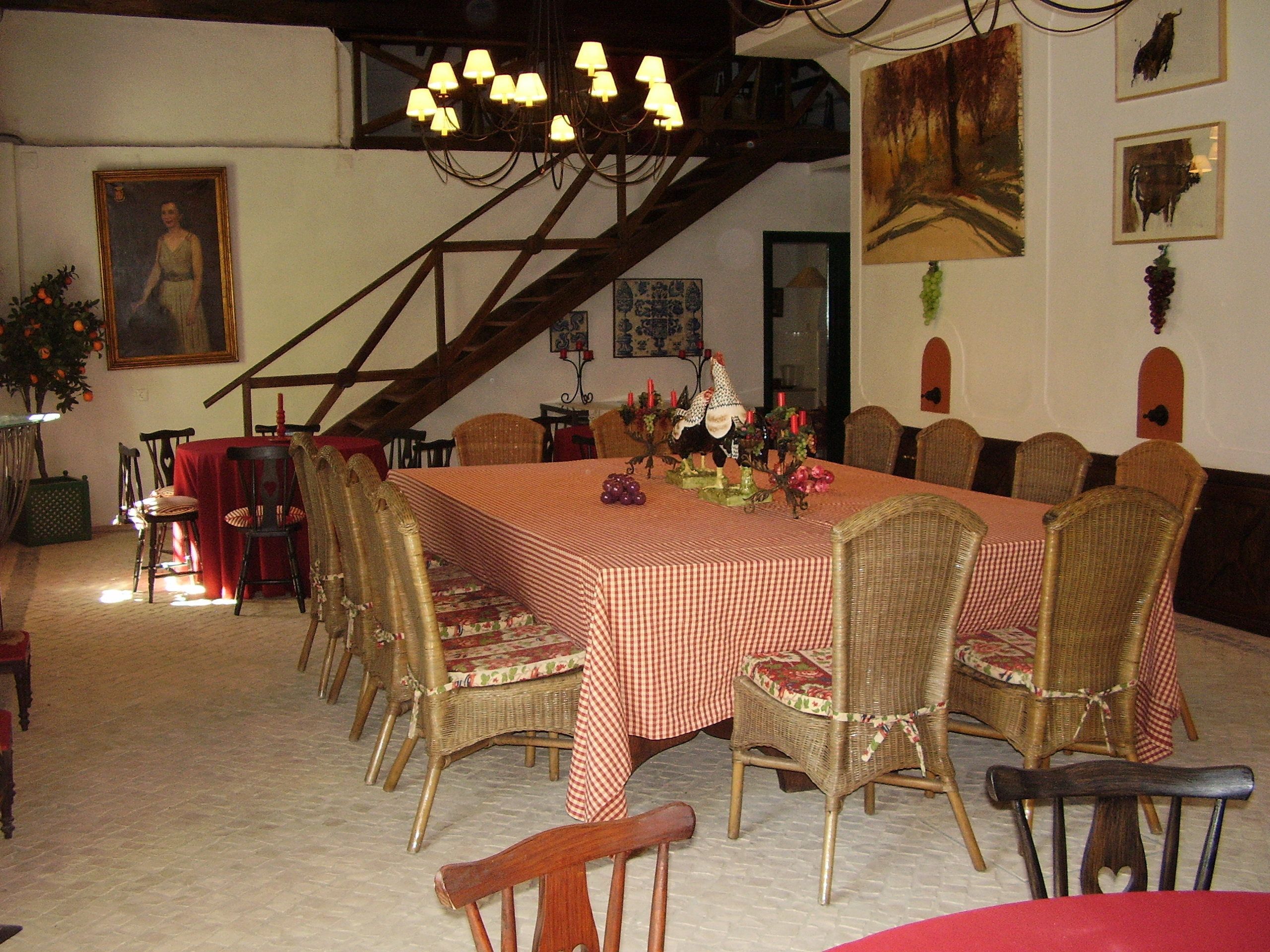 Zona de dinar amb una taula gran de quadres, cadires de vimetla, un candelabro i obres d'art a les parets.