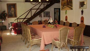 Zona de dinar amb una taula gran de quadres, cadires de vimetla, un candelabro i obres d'art a les parets.