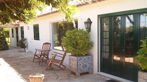 A stone-paved patio with a wooden table and chairs, a potted plant, and a traditional door with a window. - Quinta do Casalinho (Almeirim)