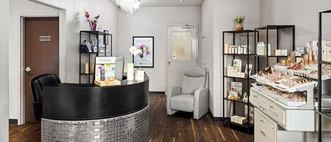 A reception area with a black reception desk, a white armchair, and shelves with various products.
