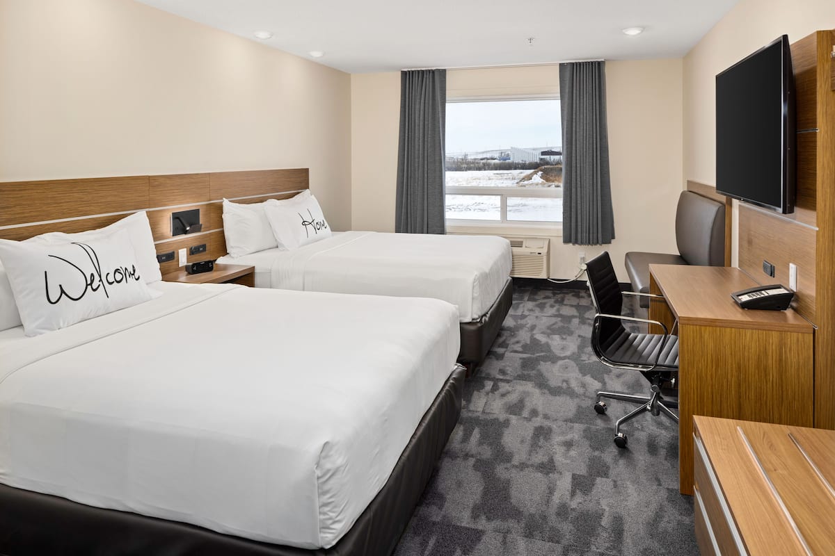 A hotel room with two beds, a desk, a chair, a TV, and a window with curtains.