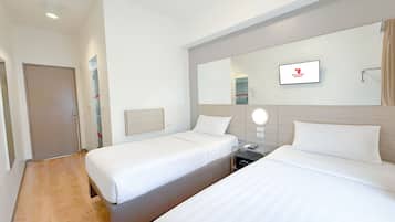 A hotel room with two single beds, a bedside table with a lamp, a mirror, and a wall-mounted TV.