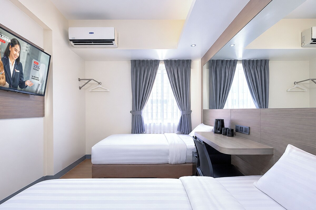 Habitación de hotel con dos camas, un escritorio, un televisor de pantalla plana, aire acondicionado y un espejo grande.