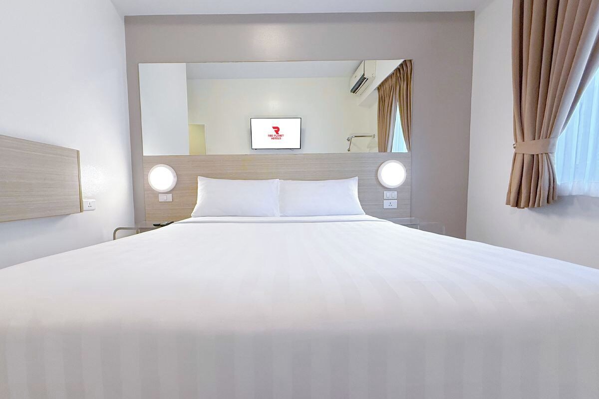 Une chambre d’hôtel avec un grand lit, une tête de lit, un miroir et un téléviseur.
