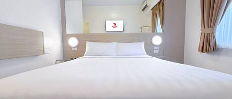 A hotel room with a large bed, two bedside tables, a round mirror, and a television on the wall.