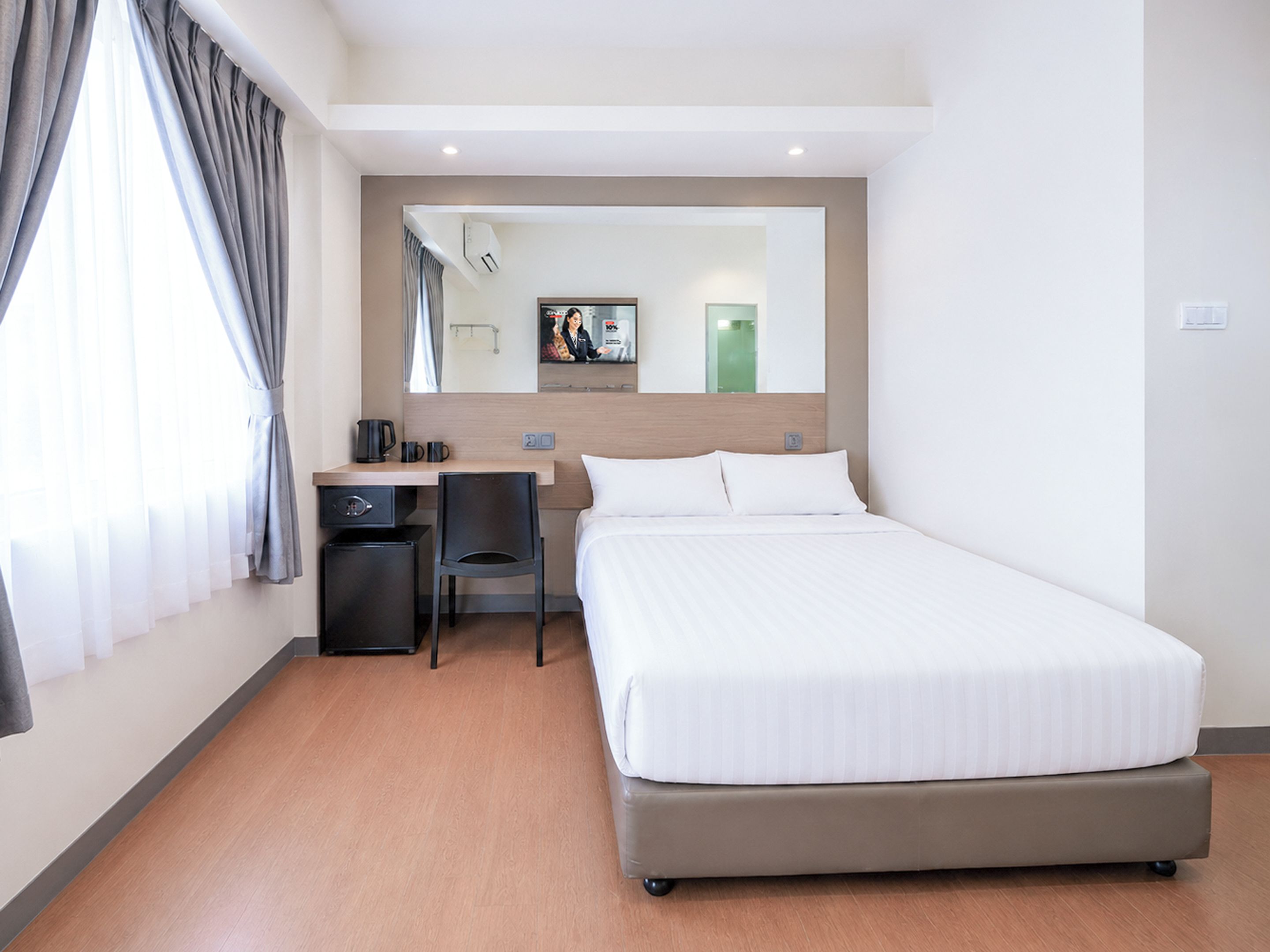 A hotel room with a bed, a desk, a chair, a television, and a window with curtains.