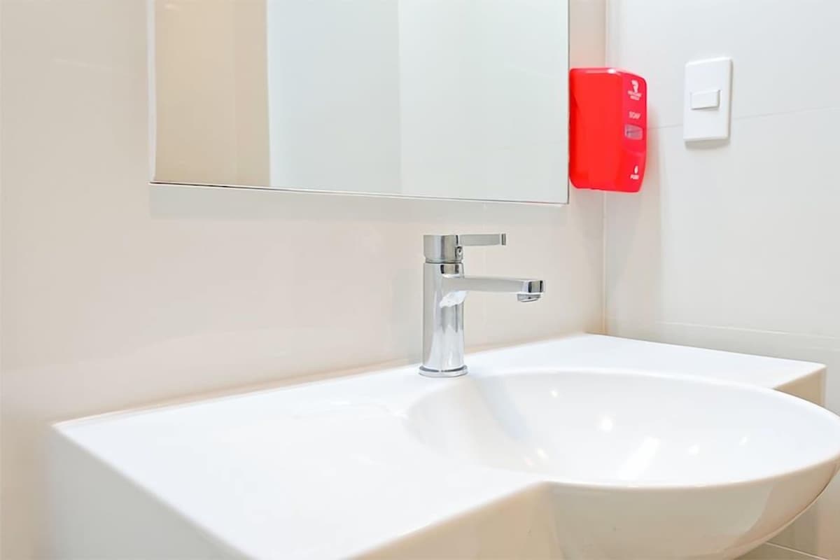Un baño moderno con un lavamanos blanco, grifo cromado y dispensador de jabón rojo.