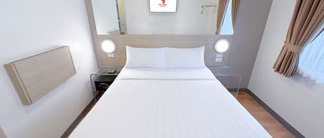 Habitación de hotel con una cama grande, una mesita de noche con lámpara, un espejo y un televisor montado en la pared.