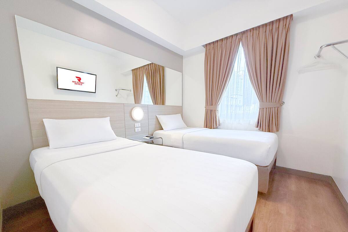 A hotel room with two beds, a mirror, a TV, and a window with curtains.