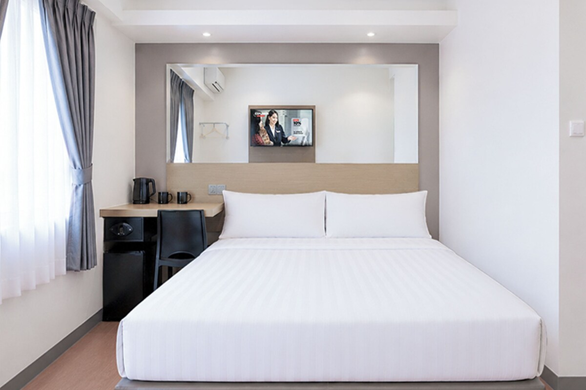 Una habitación de hotel con una cama grande, un escritorio con una silla, una cafetera y un espejo.
