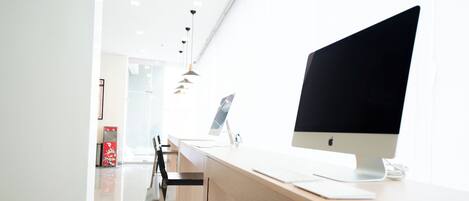 Un espacio de oficina moderno con una gran iMac de Apple sobre un escritorio, un separador de vidrio y un diseño minimalista.
