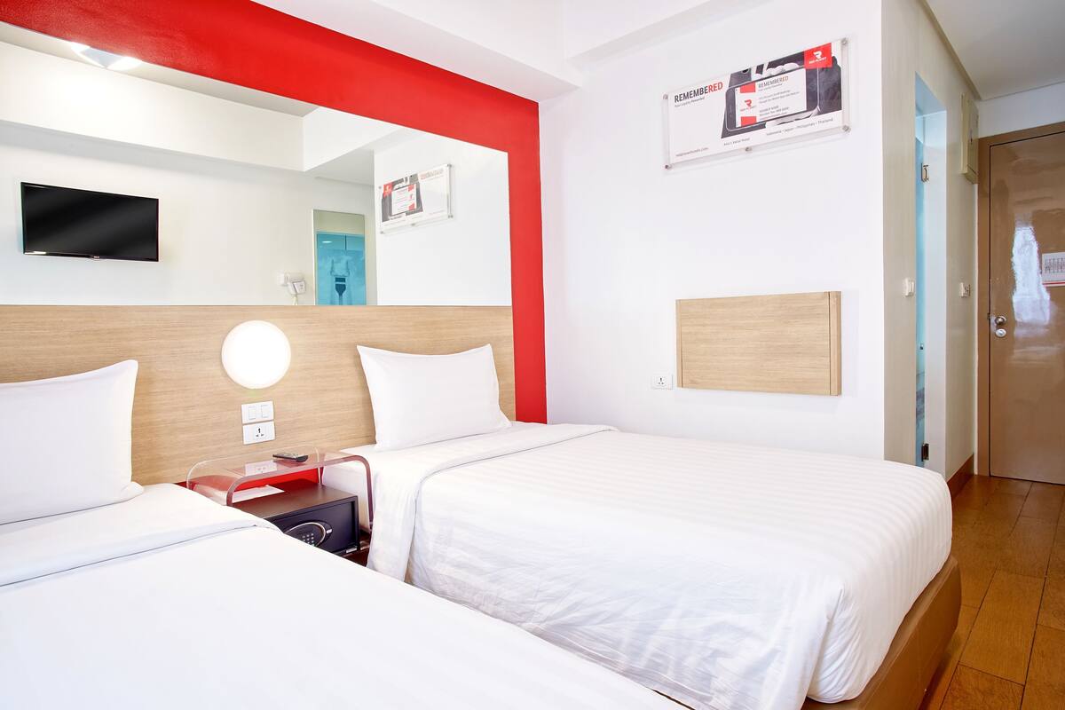 A hotel room with two beds, a TV, a mirror, and a red accent wall.
