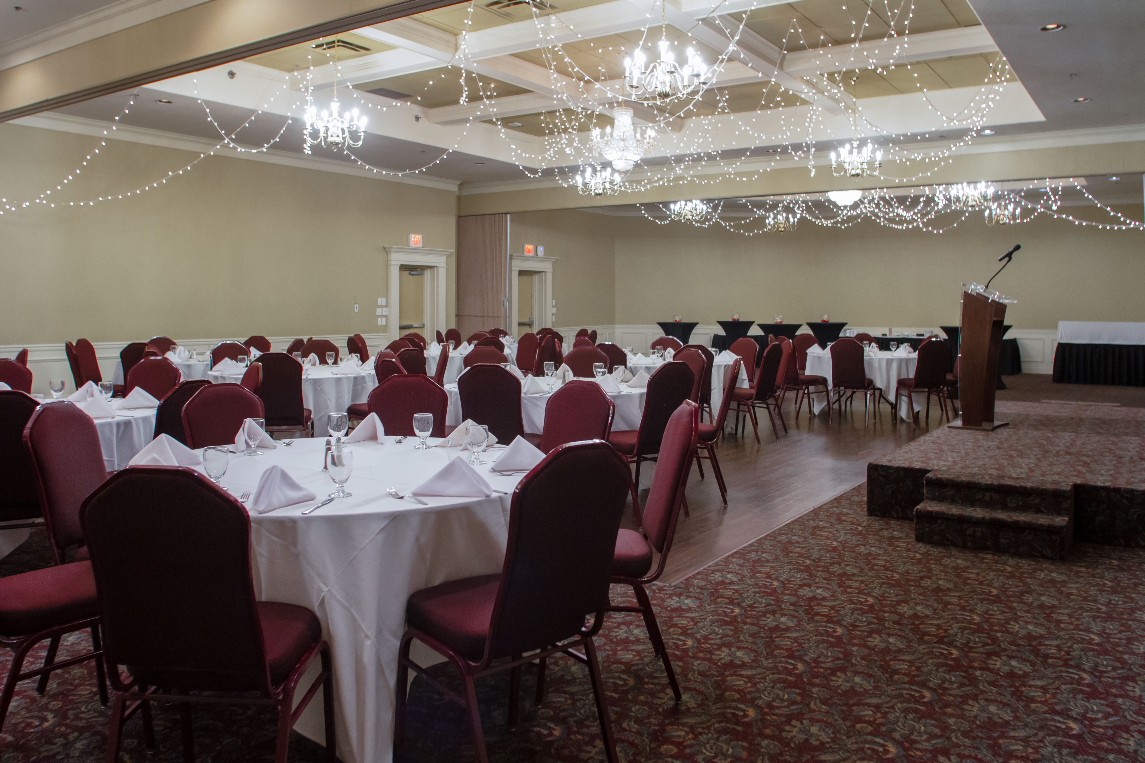 A banquet hall with round tables, red chairs, and a stage with a podium.