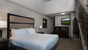 Una habitación de hotel con una cama grande, un escritorio, un televisor y una escalera.