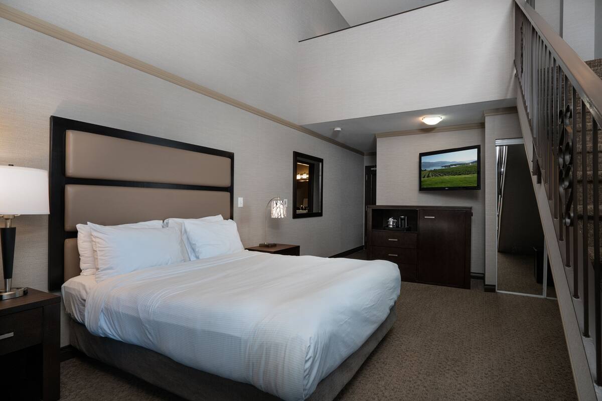 A hotel room with a large bed, a desk, a television, and a staircase.