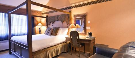 A four-poster bed with a headboard, a desk with a chair, and a leather sofa in a hotel room.