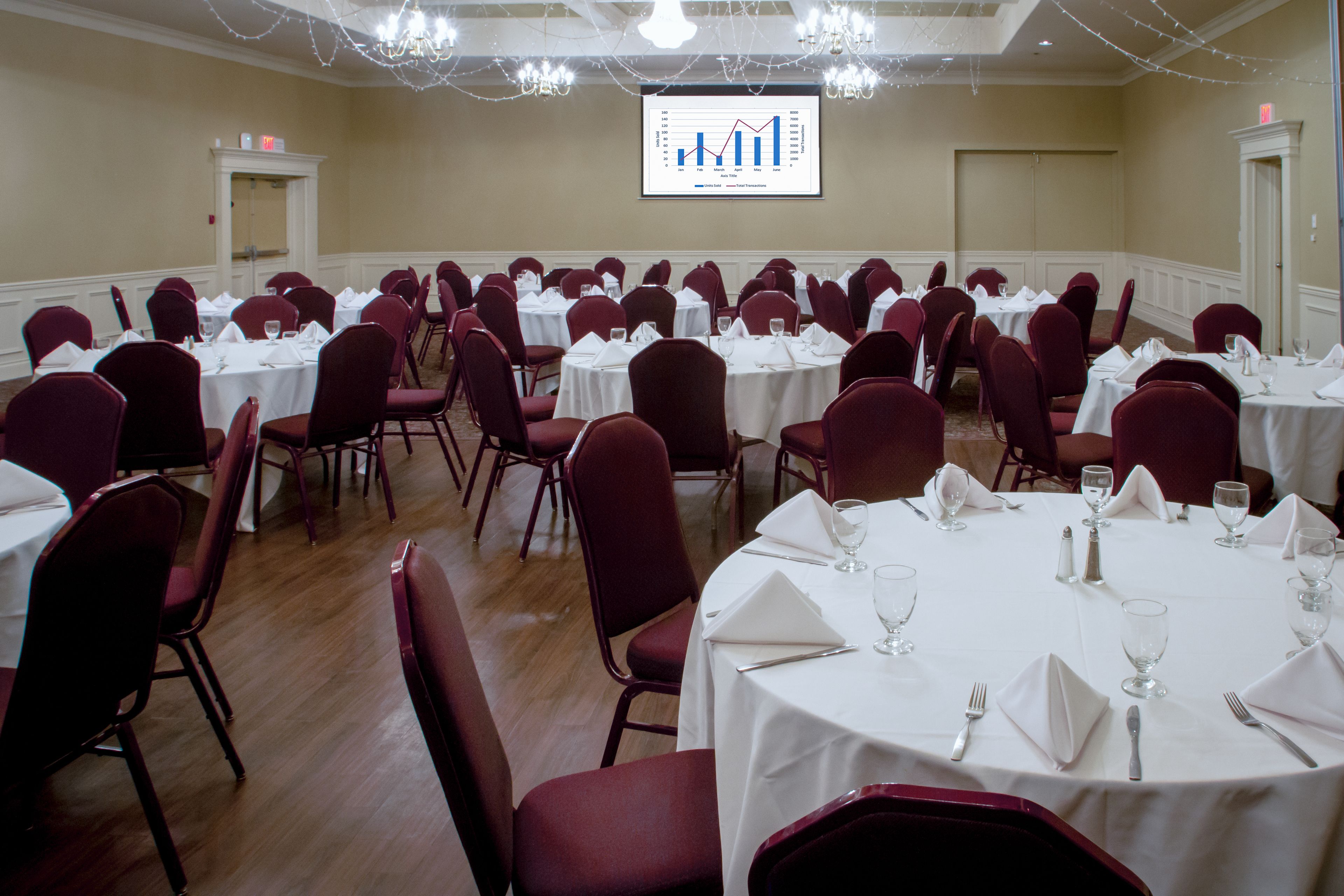 A conference room with multiple round tables, each set with white tablecloths, red chairs, and glassware.