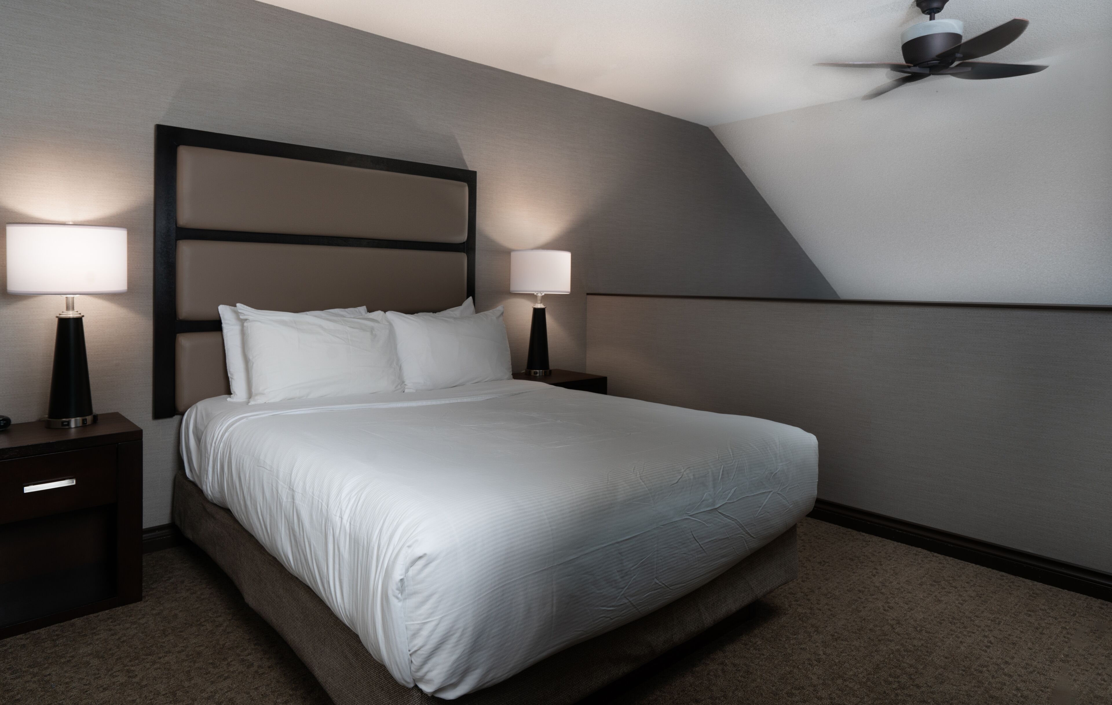 A hotel room with a large bed, two bedside tables with lamps, a ceiling fan, and a modern design.
