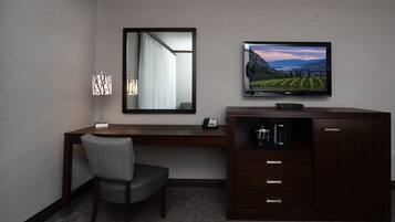 A hotel room with a desk, chair, television, and a cabinet.
