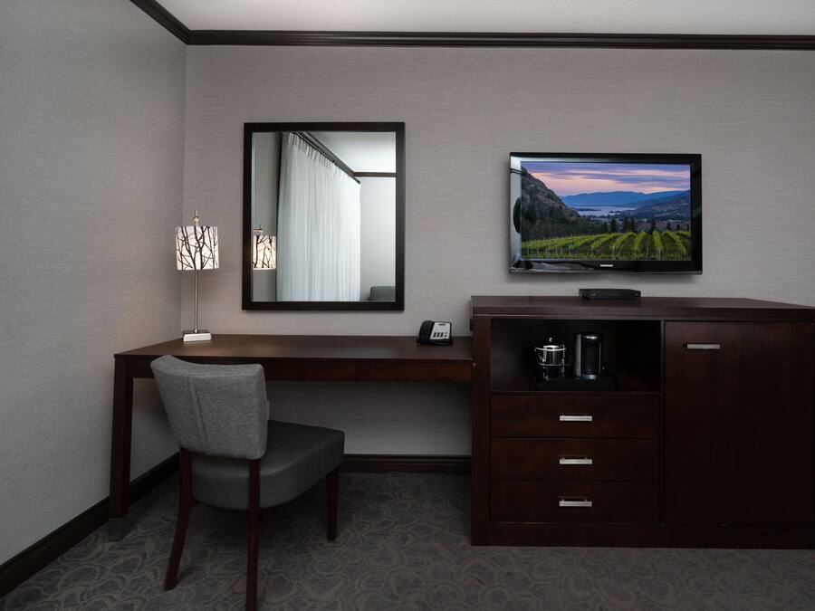 A hotel room with a desk, chair, television, and a cabinet.